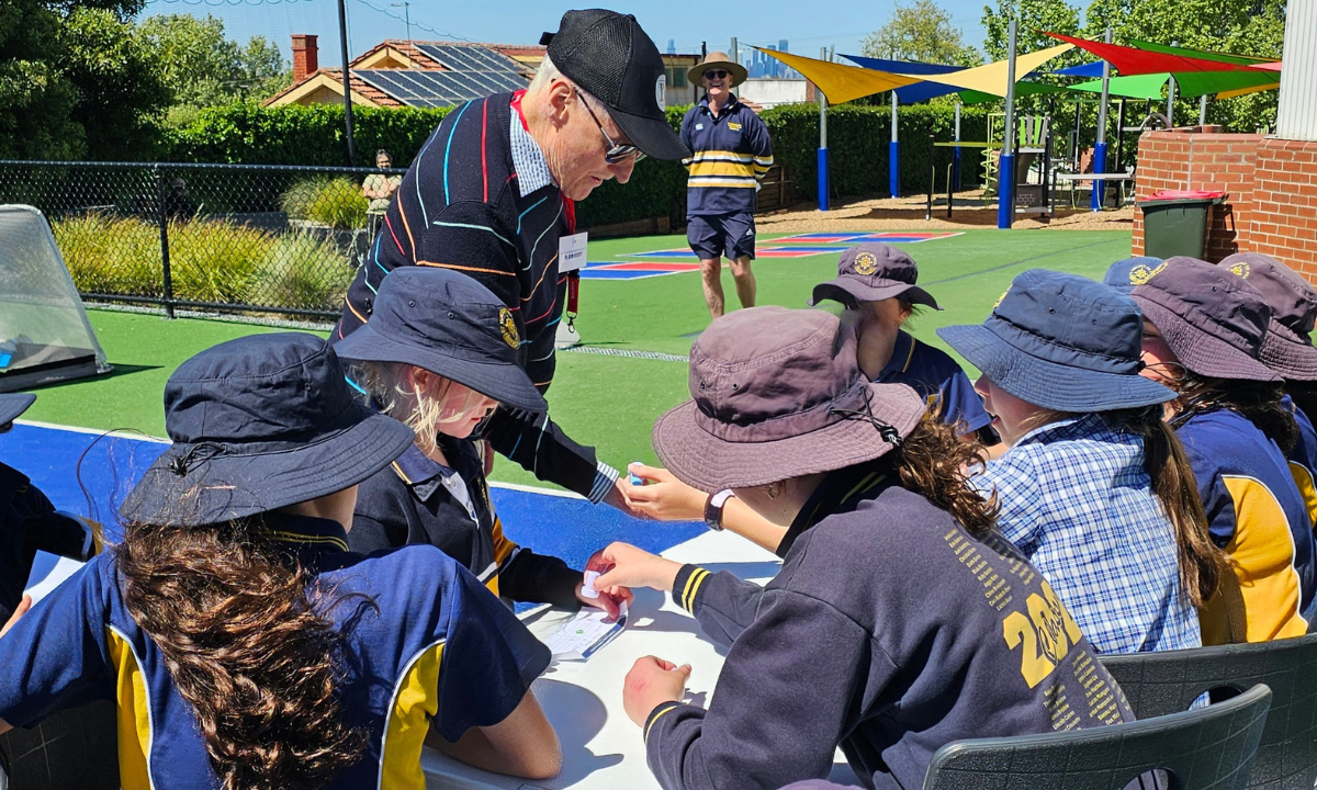 Columban Fr John Hegerty gets his stamp from the Mini  Vinnies while Principal Shane Byrne looks on.  Photo: Jacqui Russell