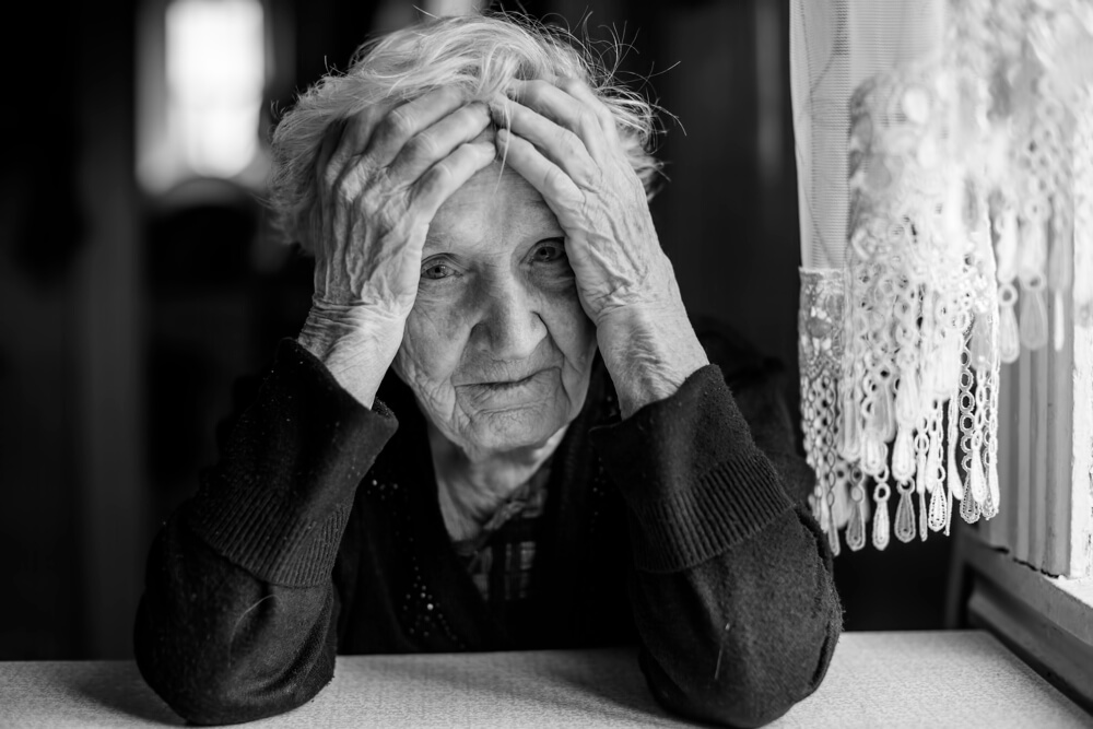 An elderly woman sitting at a table in a depressed state. Photo: De Visu/shutterstock.com