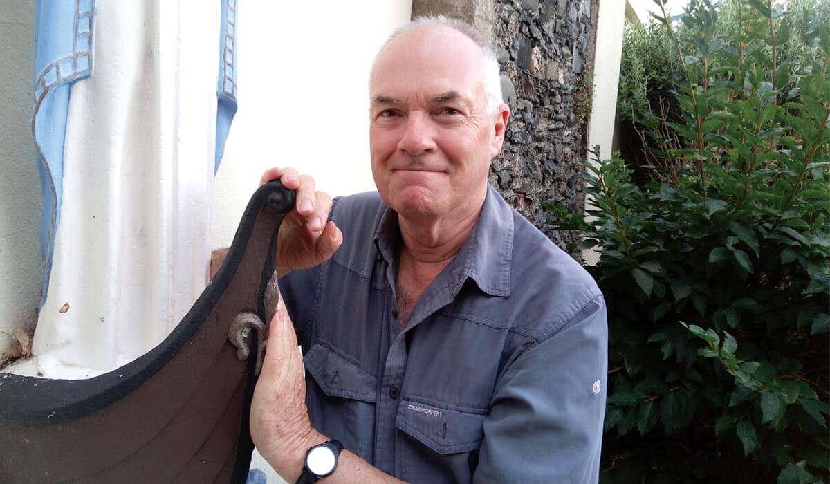 Fr John Boles beside the 'oar-less coracle', symbl of St. Maughold, outside the church in Ramsey. - Photo: Fr John Boles SSC