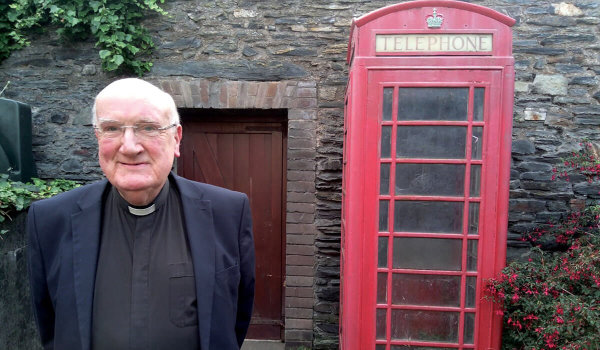Parish priest Fr Brian O'Mahoney and his beloved K6 red telephone box beside the church wall. - Photo: Fr John Boles SSC
